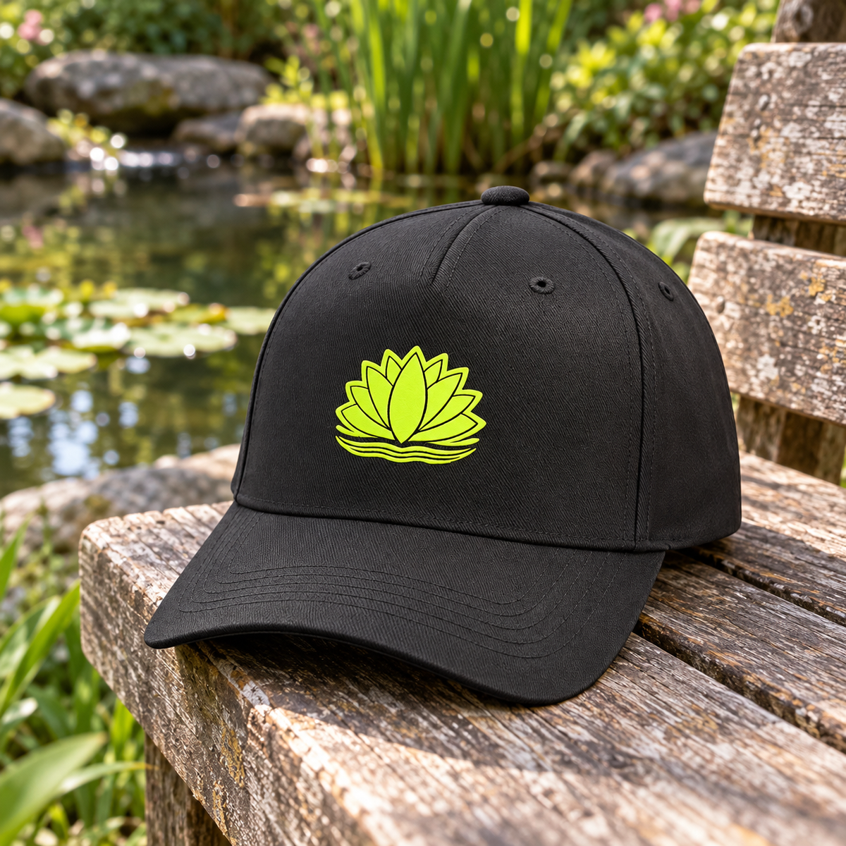 Mise en situation générée : casquette noire Aquiflor au motif nénuphar sur un banc près du bassin.